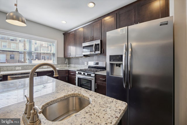 kitchen featuring light stone counters, sink, hanging light fixtures, and stainless steel appliances