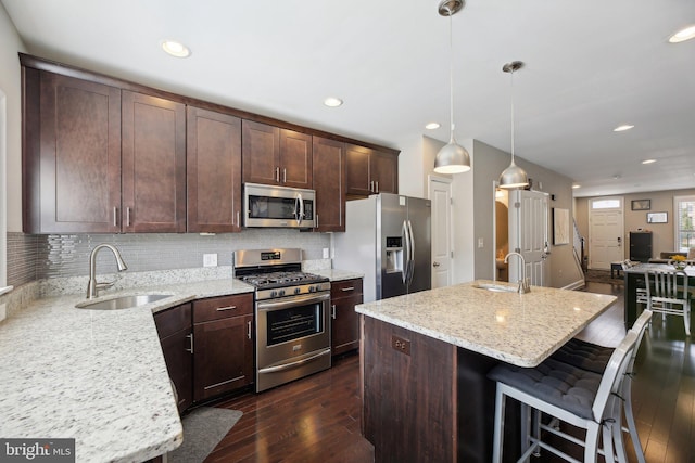 kitchen with appliances with stainless steel finishes, a kitchen island, sink, hanging light fixtures, and light stone counters