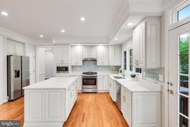 kitchen featuring a kitchen island, white cabinetry, stainless steel appliances, light wood-type flooring, and crown molding