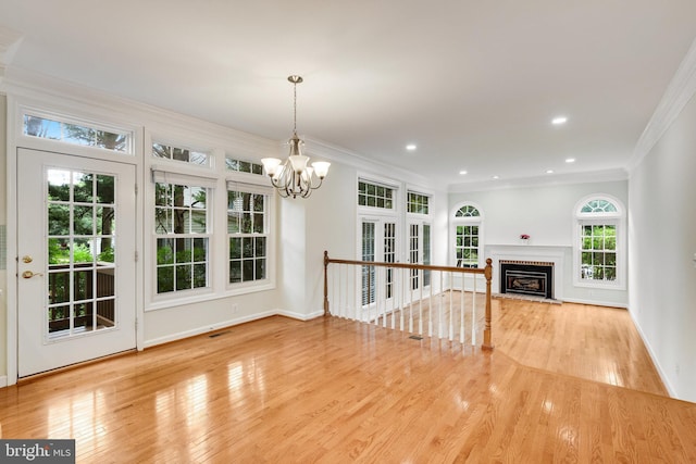 unfurnished living room featuring an inviting chandelier, crown molding, and light hardwood / wood-style floors