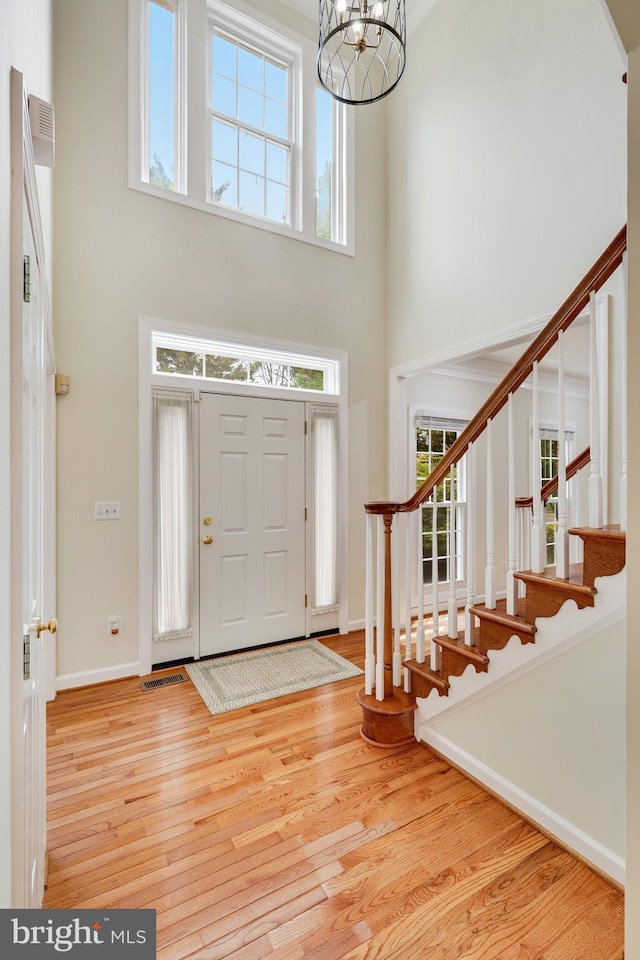 entryway with a towering ceiling, a chandelier, and light hardwood / wood-style floors