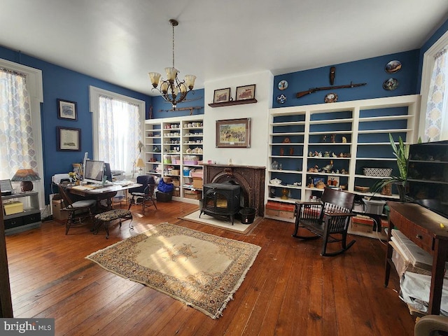 home office with a wood stove, an inviting chandelier, and wood-type flooring