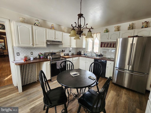 kitchen featuring radiator heating unit, hardwood / wood-style floors, appliances with stainless steel finishes, white cabinets, and decorative light fixtures