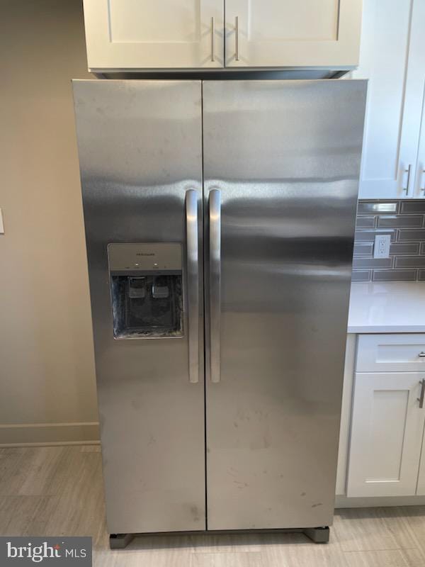 details featuring stainless steel fridge with ice dispenser, backsplash, and white cabinets