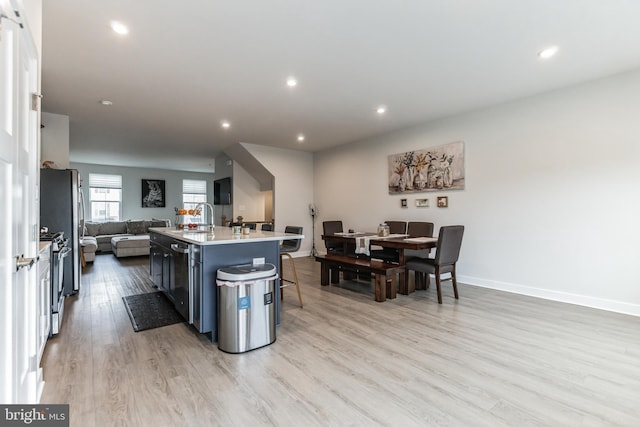 kitchen featuring a kitchen bar, an island with sink, stainless steel appliances, light wood-type flooring, and sink