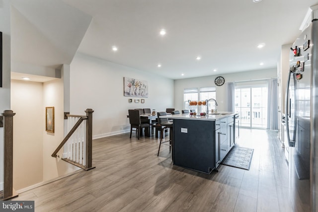 kitchen featuring a kitchen breakfast bar, wood-type flooring, stainless steel fridge, and a center island with sink