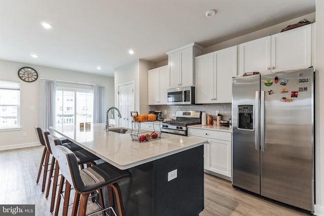 kitchen featuring white cabinets, a kitchen bar, stainless steel appliances, an island with sink, and light wood-type flooring