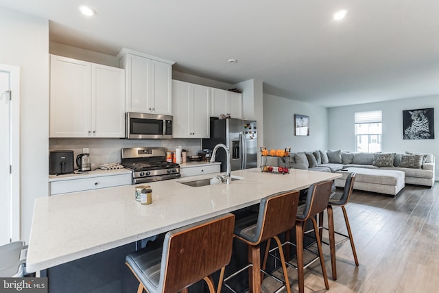 kitchen featuring a kitchen bar, white cabinetry, stainless steel appliances, an island with sink, and sink