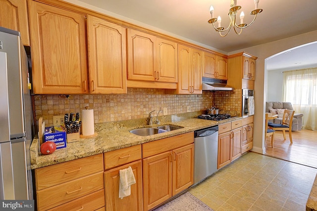 kitchen with stainless steel appliances, decorative backsplash, sink, a notable chandelier, and light stone counters