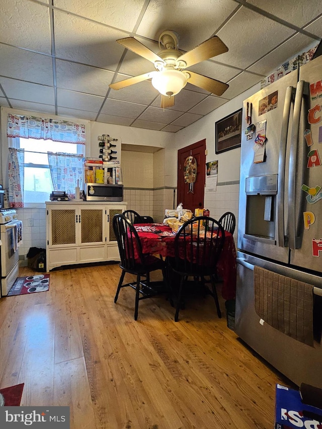 dining space with tile walls, a drop ceiling, ceiling fan, and light hardwood / wood-style flooring