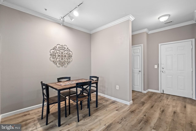 dining area with crown molding, rail lighting, and light hardwood / wood-style flooring