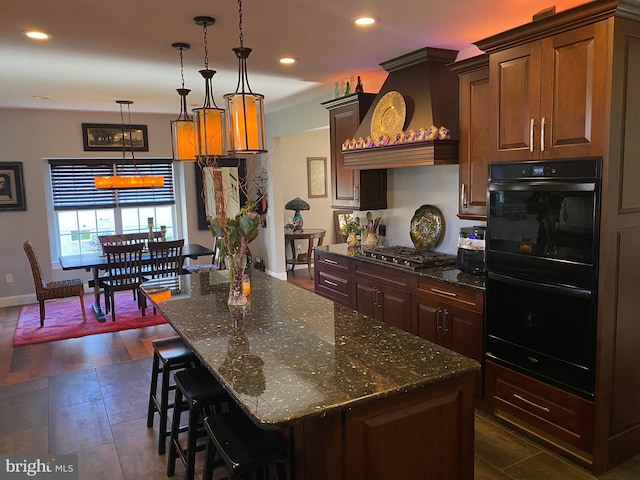 kitchen with black double oven, custom exhaust hood, stainless steel gas cooktop, a kitchen island, and pendant lighting