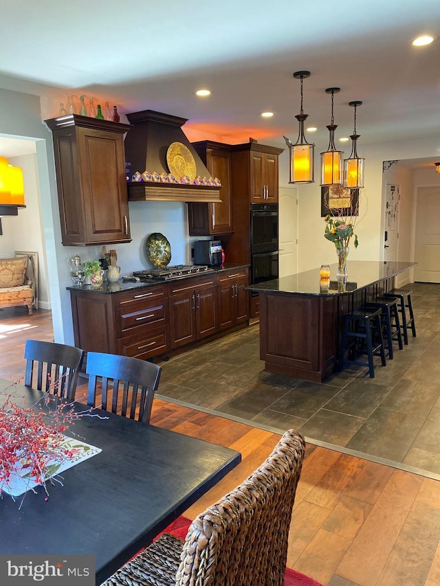 kitchen featuring a center island, black double oven, stainless steel gas cooktop, custom range hood, and a breakfast bar area