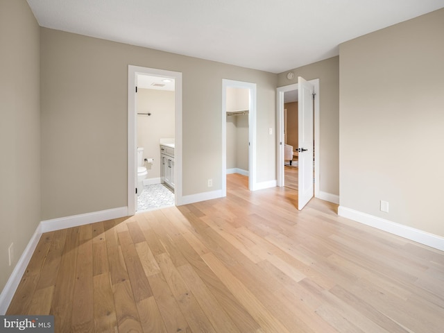 unfurnished bedroom featuring ensuite bathroom, a walk in closet, light hardwood / wood-style floors, and a closet