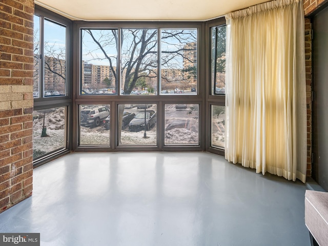 empty room featuring brick wall, plenty of natural light, and concrete flooring