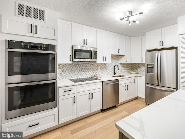 kitchen with sink, white cabinetry, light wood-type flooring, stainless steel appliances, and backsplash