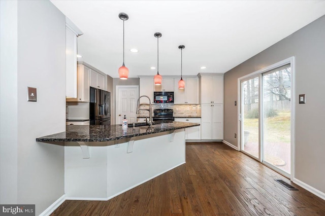 kitchen featuring a breakfast bar area, white cabinetry, hanging light fixtures, kitchen peninsula, and black appliances