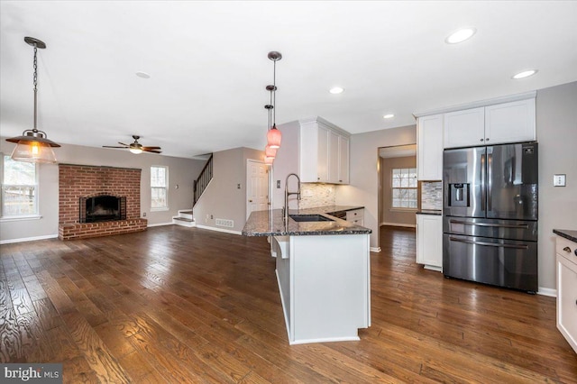 kitchen with decorative light fixtures, sink, dark stone countertops, white cabinets, and stainless steel fridge