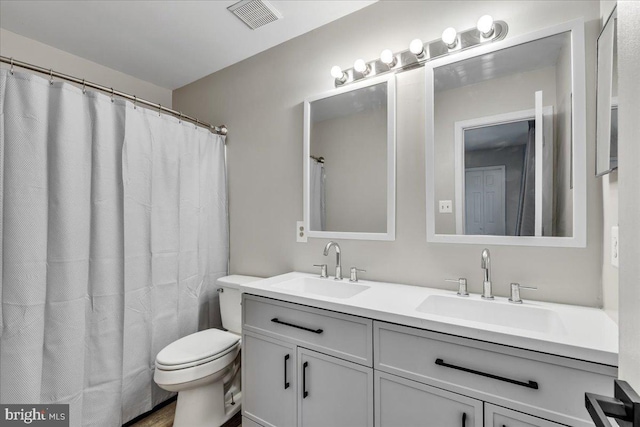 full bath featuring toilet, double vanity, visible vents, and a sink