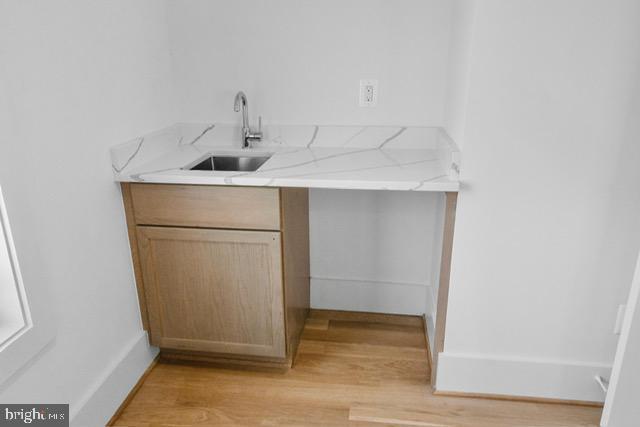 bar with light stone countertops, sink, light brown cabinetry, and light hardwood / wood-style flooring