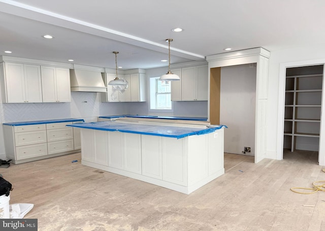 kitchen featuring custom exhaust hood, backsplash, pendant lighting, light hardwood / wood-style flooring, and a center island