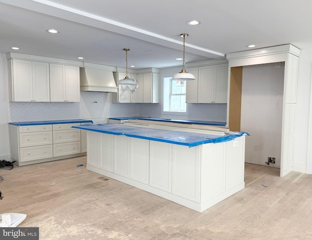 kitchen featuring premium range hood, decorative light fixtures, a center island, light hardwood / wood-style floors, and backsplash