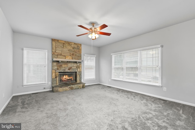 unfurnished living room featuring a stone fireplace, ceiling fan, and carpet