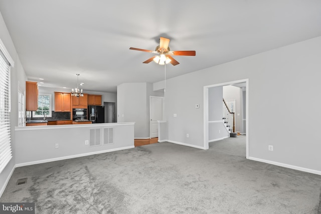 unfurnished living room with sink, carpet flooring, and ceiling fan with notable chandelier