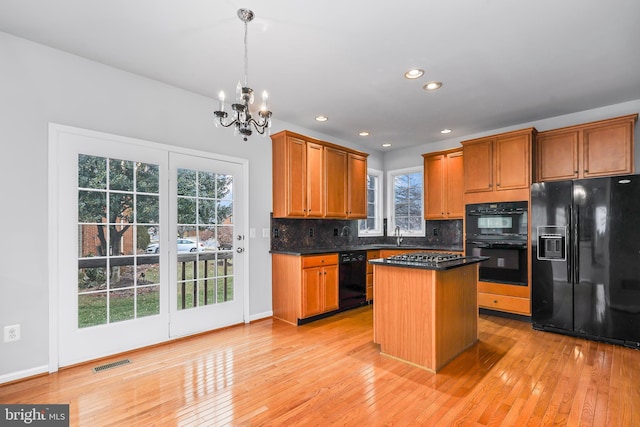 kitchen with hanging light fixtures, light wood-type flooring, a kitchen island, decorative backsplash, and black appliances