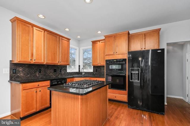 kitchen featuring sink, tasteful backsplash, light wood-type flooring, a kitchen island, and black appliances