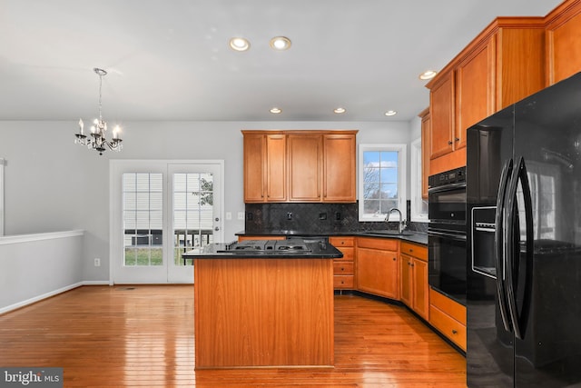 kitchen featuring sink, a center island, tasteful backsplash, black appliances, and light wood-type flooring