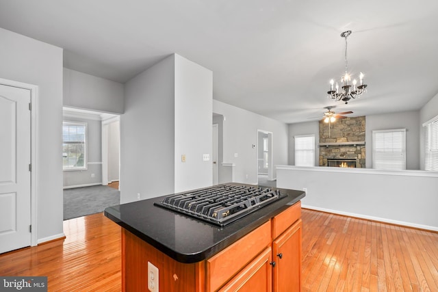 kitchen featuring a stone fireplace, a kitchen island, pendant lighting, stainless steel gas stovetop, and light hardwood / wood-style floors