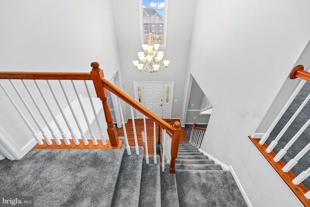 stairs with a chandelier, carpet floors, and a high ceiling