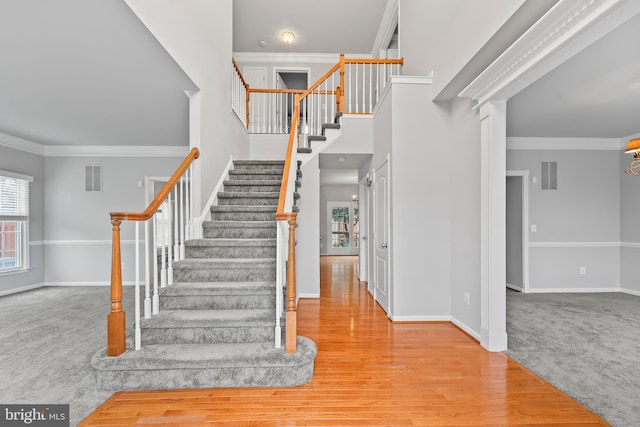 staircase with hardwood / wood-style flooring, a towering ceiling, and ornamental molding