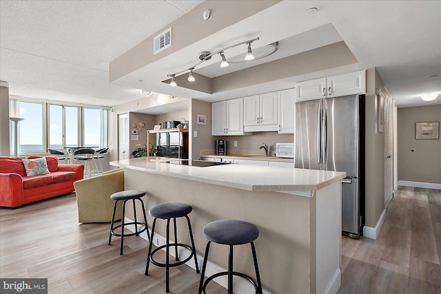 kitchen featuring white cabinets, stainless steel fridge, a spacious island, and a kitchen bar