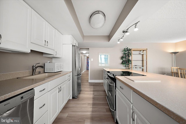 kitchen with a raised ceiling, sink, white cabinetry, light wood-type flooring, and appliances with stainless steel finishes