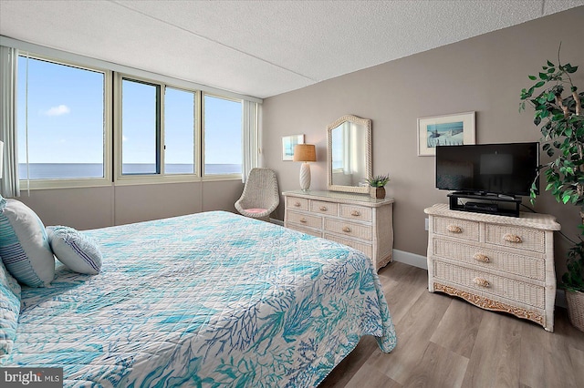 bedroom with a textured ceiling, a water view, and light wood-type flooring