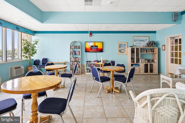 dining room with light tile patterned flooring, a wall mounted AC, and a drop ceiling