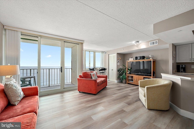 living room featuring a textured ceiling, a wall of windows, light hardwood / wood-style flooring, and a water view