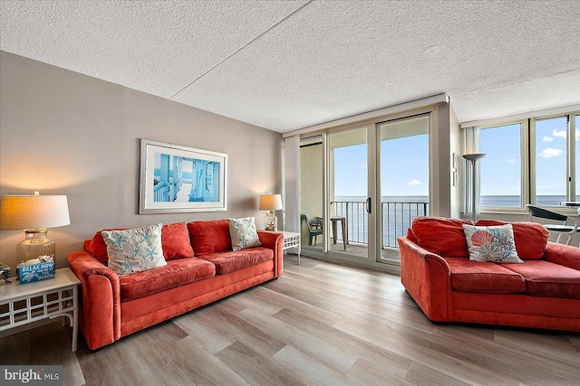 living room featuring a water view, a wall of windows, a textured ceiling, and light hardwood / wood-style floors