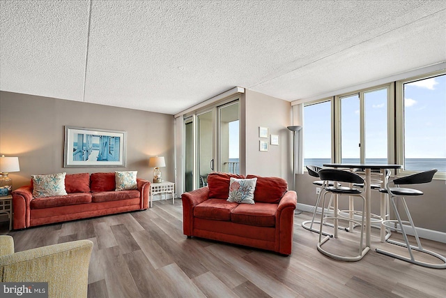 living room with a textured ceiling, floor to ceiling windows, a water view, and light wood-type flooring