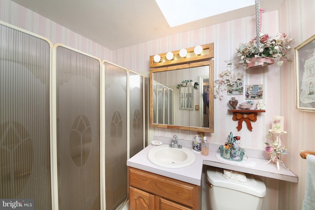 bathroom with toilet, a skylight, vanity, a shower with door, and wallpapered walls