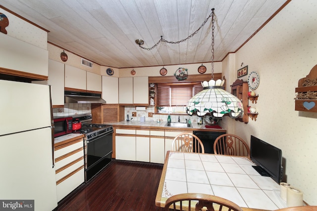 kitchen with under cabinet range hood, white cabinetry, tile counters, freestanding refrigerator, and range with gas cooktop