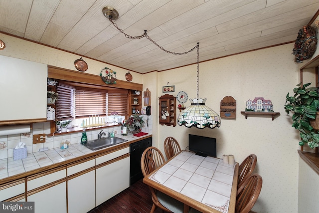 kitchen featuring tile countertops, a sink, white cabinetry, black dishwasher, and wallpapered walls