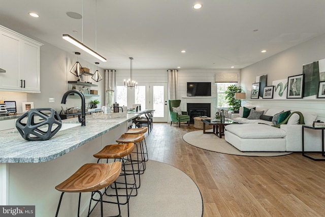 kitchen with white cabinetry, a breakfast bar area, decorative light fixtures, light stone countertops, and light hardwood / wood-style flooring