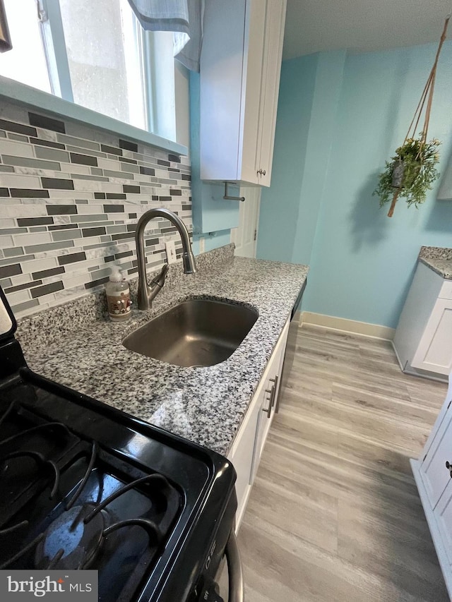 kitchen with sink, white cabinets, backsplash, light stone countertops, and black range with gas cooktop