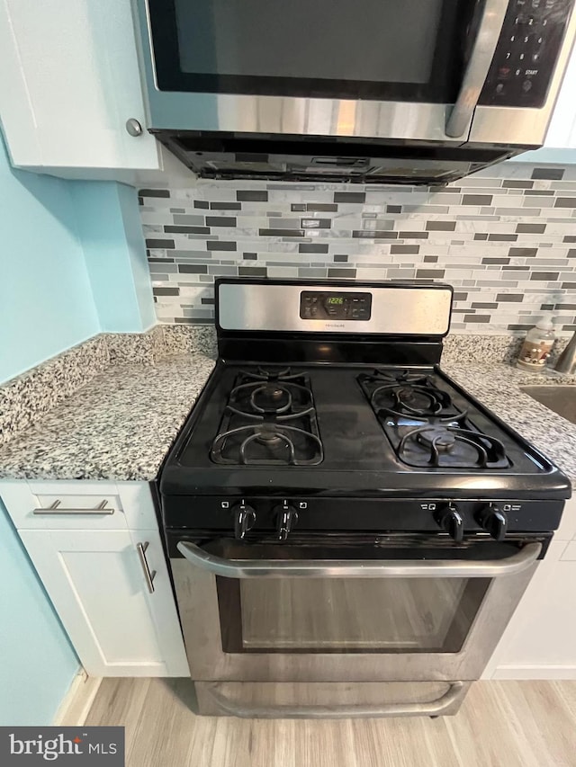 kitchen with stainless steel appliances, white cabinetry, light stone countertops, and light hardwood / wood-style flooring