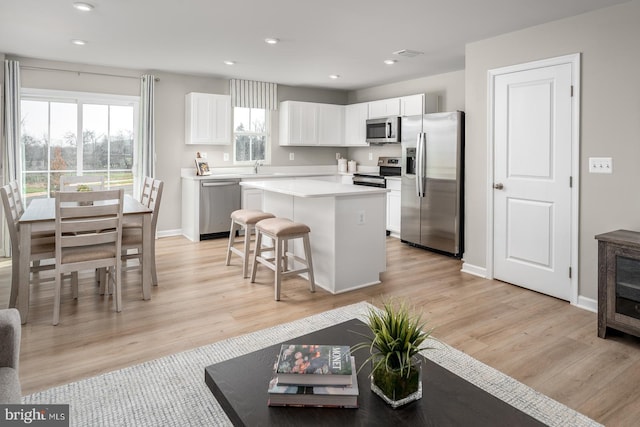 kitchen with white cabinets, a center island, stainless steel appliances, light hardwood / wood-style flooring, and a breakfast bar area