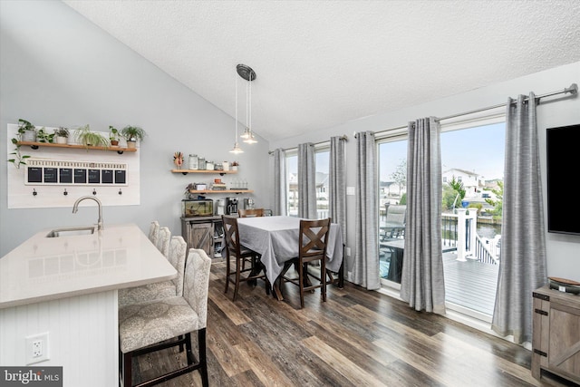 dining room with sink, dark wood-type flooring, a textured ceiling, and vaulted ceiling