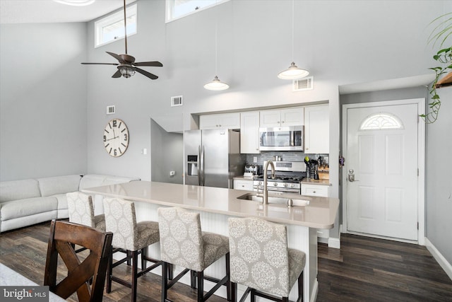 kitchen with tasteful backsplash, hanging light fixtures, white cabinets, sink, and stainless steel appliances